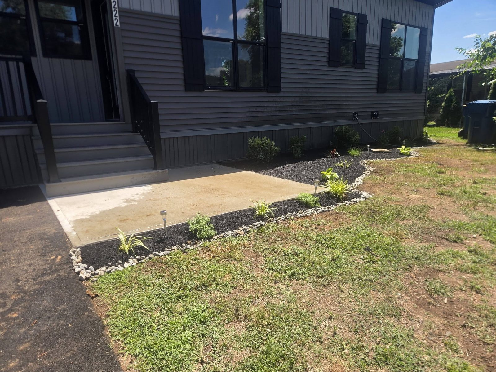 New concrete patio framed by black mulch beds and a river rock border