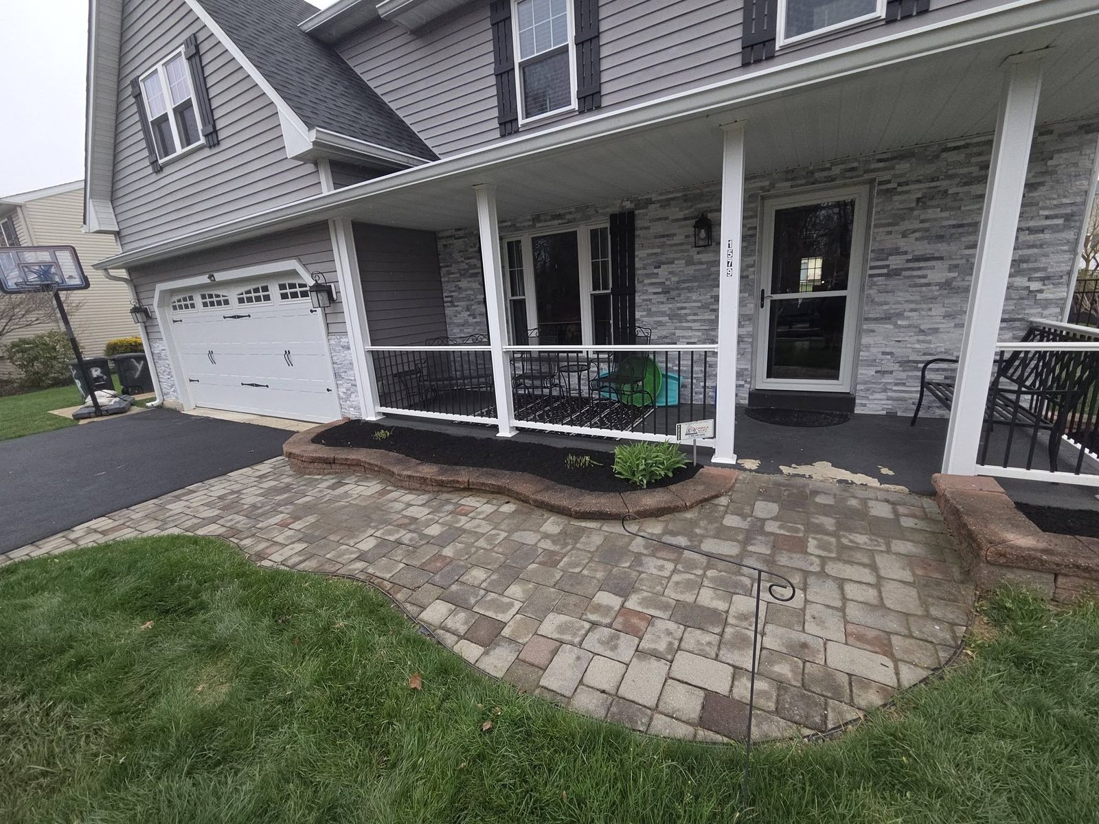Front porch bed edged in black mulch beside a paver walkway