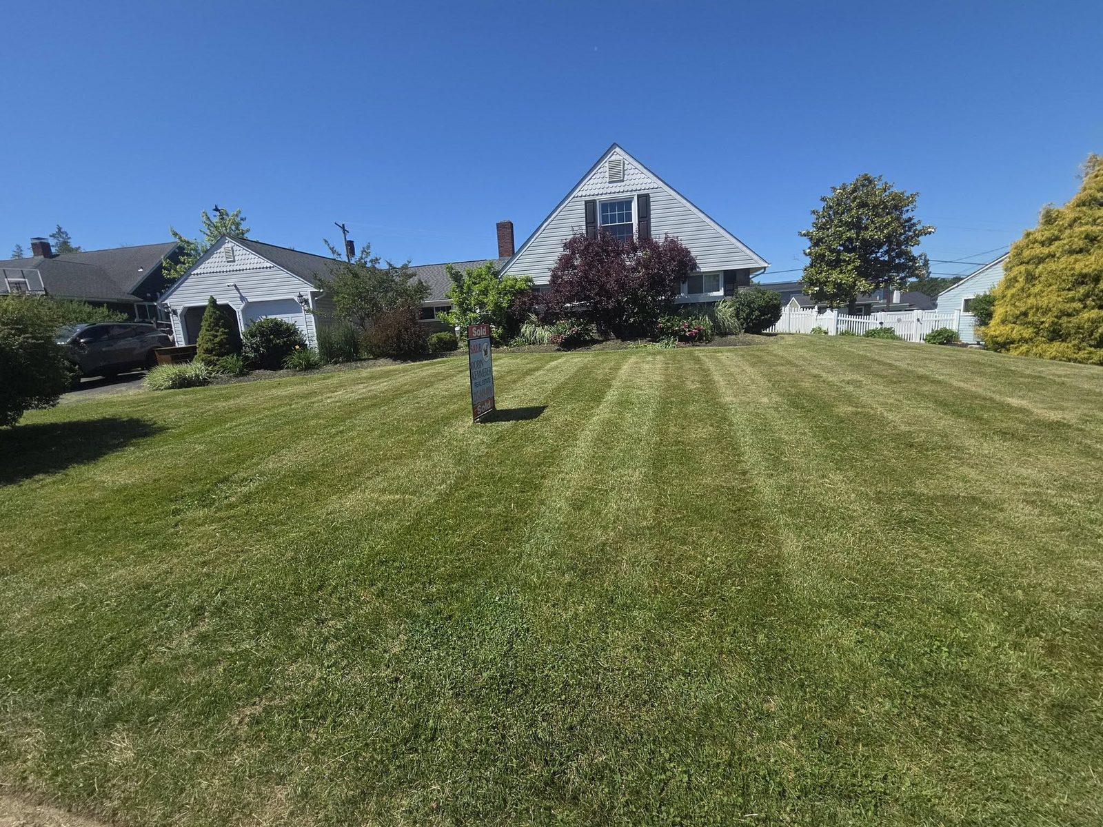 Striped front lawn at a listed home with a sold sign in the yard